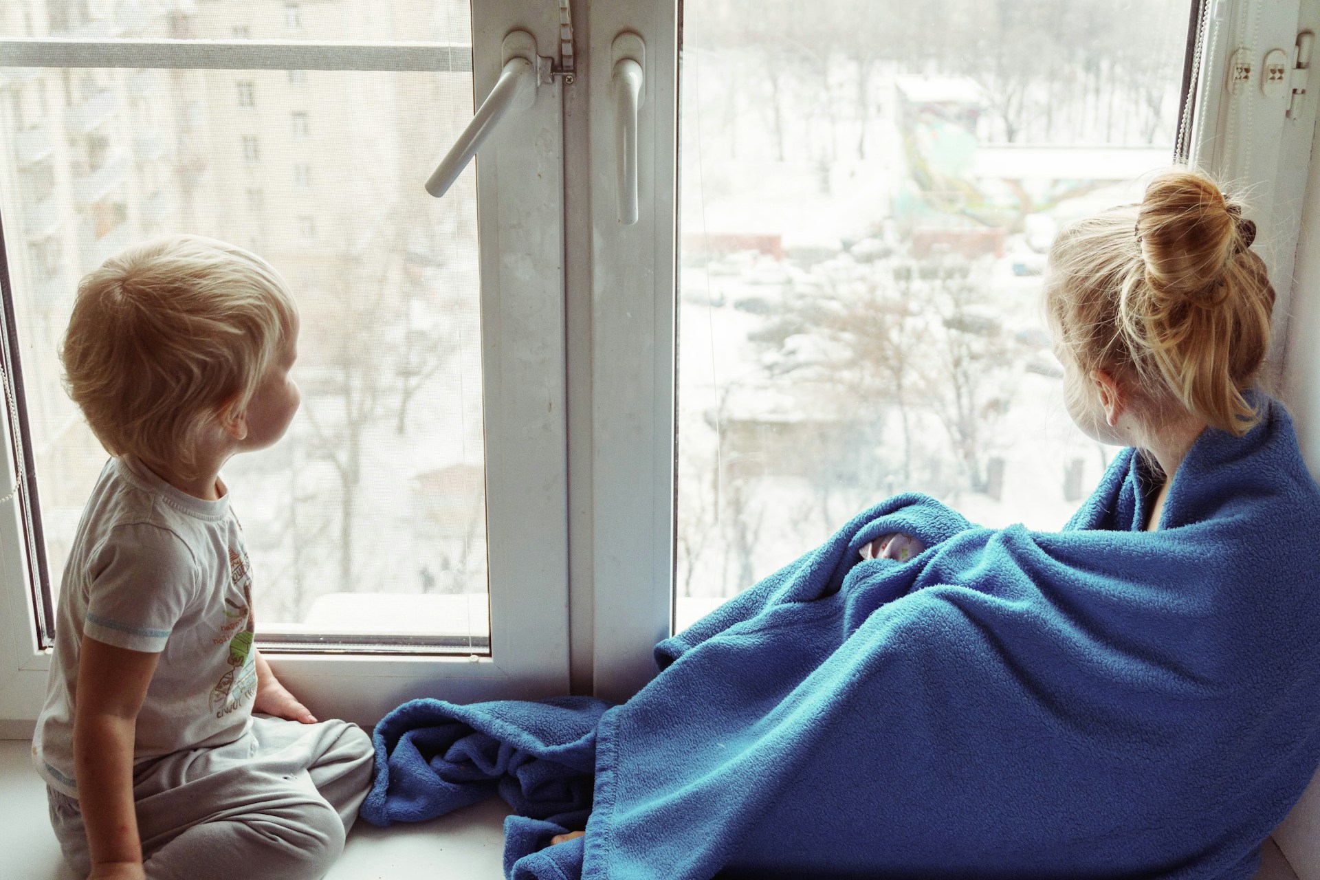 Two toddlers looking out a small apartment window